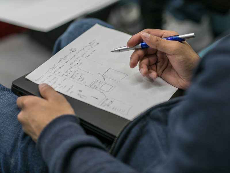 Plano detalle de las manos de un estudiante mientras toma apuntes en una hoja de papel